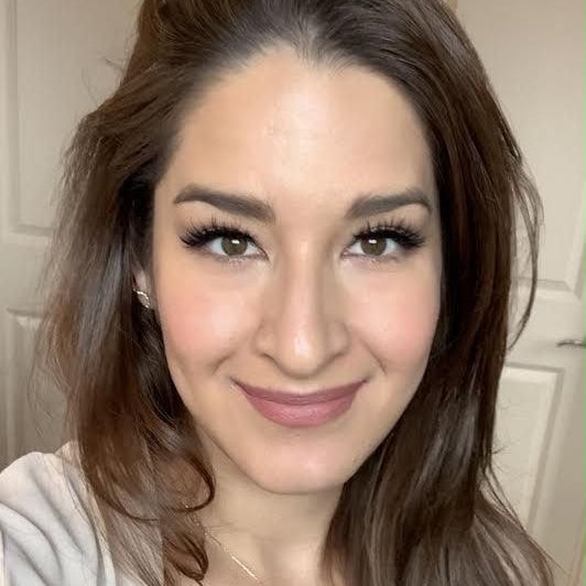 Woman with long brown hair wearing a beige top indoors.